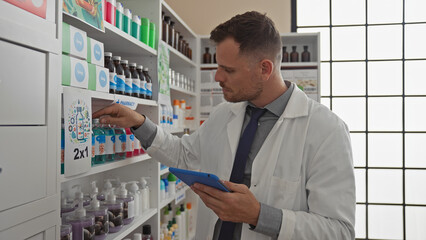 A male pharmacist examines products on a shelf in a modern pharmacy while holding a tablet.