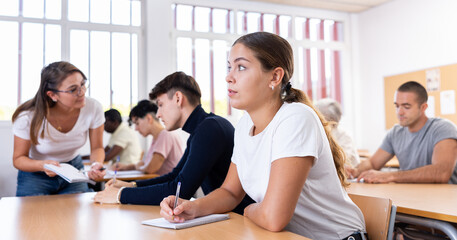 Young woman listening carefully to lecture in university. Latin woman teacher explaining information to young man sitting next to her.