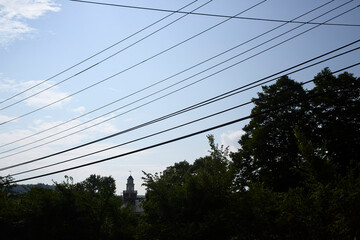 Powerline cables create a pattern in front of the blue sky with a tower in the distance flanked by a dark treeline.