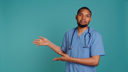 Portrait of african american nurse pointing hands towards empty space, doing advertising, talking with audience. Healthcare employee doing promotional ad, showing copy text, studio backdrop, camera B