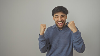 A cheerful young arab man with a beard celebrating and clenching fists against a white background