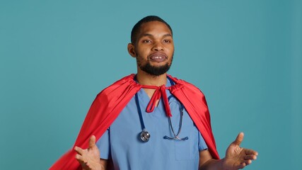 Male nurse portraying superhero showing courage and strength fighting diseases, studio backdrop. Portrait of african american doctor posing as hero in costume, holding empowering speech, camera A