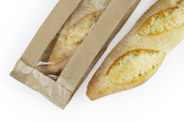Two freshly baked baguettes, one wrapped in brown paper bag, Artisan French baguettes with crispy crusts in paper packaging. Isolated on a white background. Closeup. With clipping path.