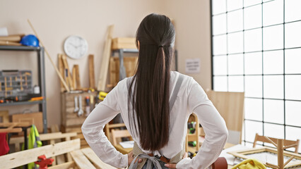 Young asian woman at work in a carpentry workshop, surrounded by wood, tools, and hardware