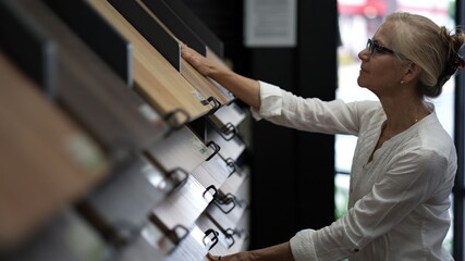 Happy mature woman running hand across solid or engineered wood plank samples in a floor or...