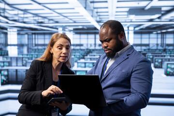 Team of programmers in server room using laptop to implement and maintain security measures,...