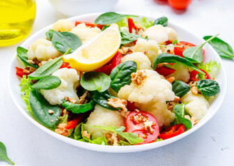 Autumn vegan salad with baked cauliflower and paprika, red tomatoes, baby spinach with walnuts on white background, top view
