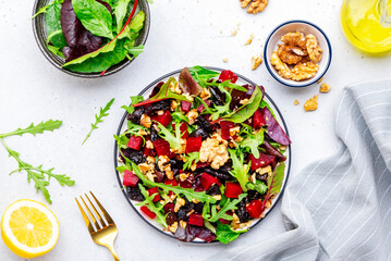 Fresh crispy vegan salad with baked beetroot, dried prunes, arugula, chard and lnuts, white background