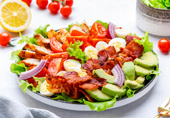 Hearty american salad with chicken meat, tomatoes, eggs, fried bacon, avocado and lettuce, gray background, top view
