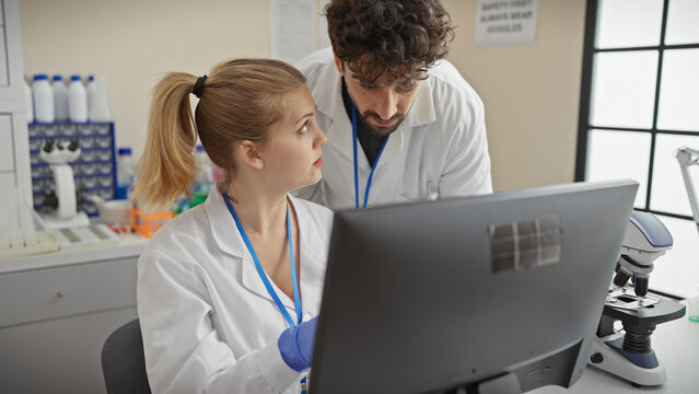 A woman and man in lab coats analyze data on a computer in a bright laboratory setting