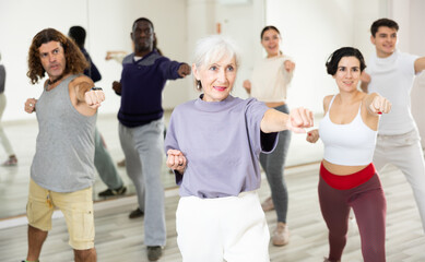 Obraz premium Happy mature woman practising modern dance moves with other people in dance studio
