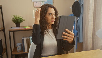 Middle-aged hispanic woman using tablet in a modern home office setting.