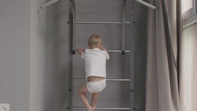 Young boy on wall doing pull-ups fun and vigor of childhood physical activities. Boy engages in sports hanging from pull-up bar on sportive wall emphasizing active and joyful aspects of childhood
