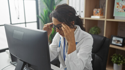 A stressed female healthcare worker at her office within a clinic, visibly overwhelmed in front of...
