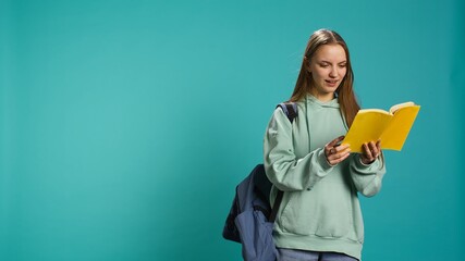 Teenage woman with book in hands showing appreciation for literature, isolated over studio background. Young reading enthusiast holding novel, enjoying reading hobby, camera B
