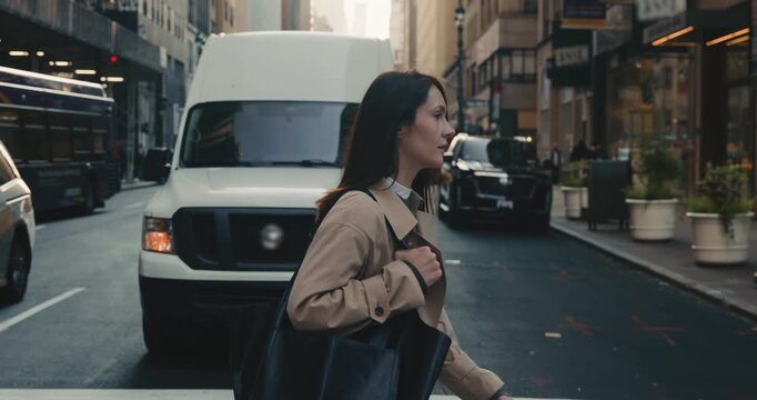 Busy attractive brunette woman crossing road in New York City with cars waiting in background