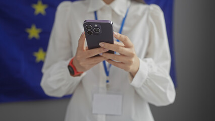 European woman using smartphone indoors with flag banner in background.