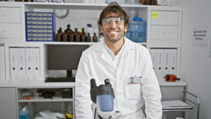 Smiling man with beard and safety glasses in white lab coat inside chemistry laboratory