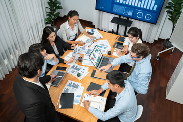 Diverse group of business analyst team analyzing financial data report. Finance data analysis chart and graph dashboard show on TV screen in meeting room for strategic marketing planning. Habiliment