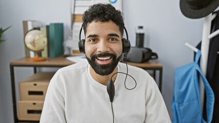 Smiling bearded man wearing headset in modern office with globe and suit on coat rack in background