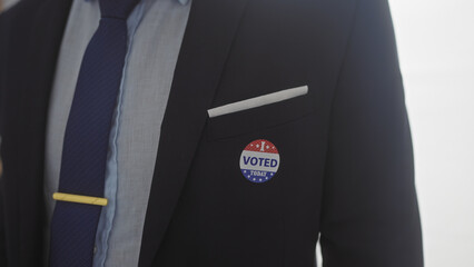 A hispanic man wearing a suit and an 'i voted' sticker signifies american democracy in an indoor...