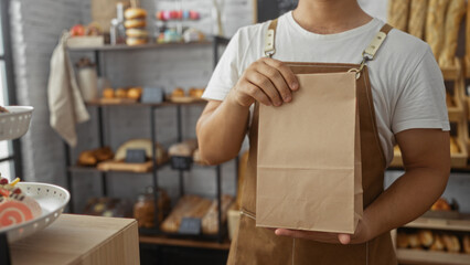 Young hispanic man holding a paper bag in a bakery shop with shelves of bread and pastries in the background