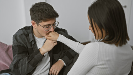 A man affectionately kisses a woman's hand, expressing love in a cozy, intimate indoor setting.