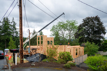 Residential house construction, boom crane lifting lumber delivery, wood support truss beams, to waiting worker 
