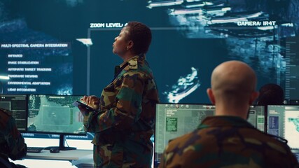 Female brigadier general conducing anti terrorism mission in military operations room, employing radar systems to detect and track enemy aircraft or missiles. Secret service program. Camera A.