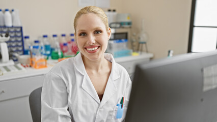 Obraz premium Smiling blonde woman in white lab coat with beakers and equipment in a laboratory setting