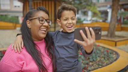 A smiling woman and boy taking a selfie together in a city park, portraying love and family in a natural outdoor setting.