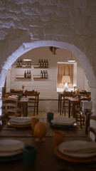 A cozy indoor italian restaurant in italy with rustic stone archways, wooden tables set with plates and cups, and shelves displaying wine bottles, creating a warm, inviting dining atmosphere.