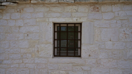 A small, barred window set in a rustic, white stone wall of an outdoor building, capturing simple architectural details.