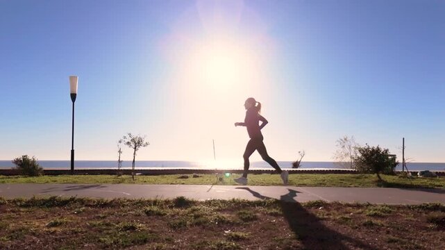 SLO MO TS WS Adult woman running in front of the Rio de la Plata. Sun backlight. Camera slides in and takes her out of frame
