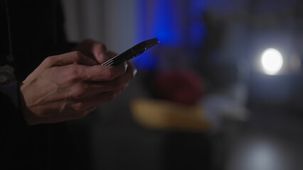 A man using smartphone in a dimly lit modern living room, conveying a sense of mystery.