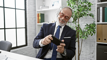 Smiling businessman in headphones using smartphone in modern office, conveying connection, technology, and corporate lifestyle.