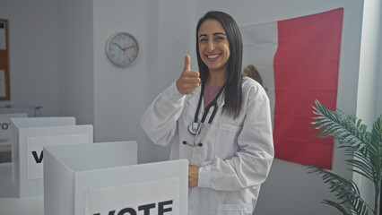 Smiling woman doctor giving thumbs-up in a voting booth with a mexican flag in the background.
