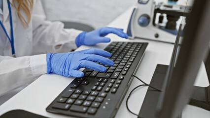 A caucasian woman scientist in a lab wearing gloves typing on a keyboard, depicting professionalism and technology.