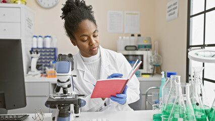 African american woman scientist reading notes in a laboratory setting with a microscope and glassware