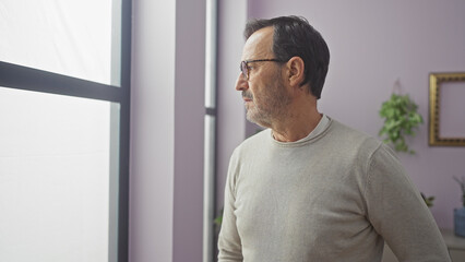 Hispanic mature man profile view indoors wearing glasses contemplating