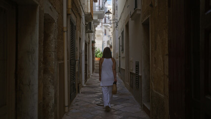 A young hispanic woman walks through the charming streets of polignano a mare in puglia, italy, capturing the essence of this beautiful european locale.