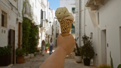 A woman holds a delicious ice cream cone while walking through the charming, narrow streets of locorotondo, puglia, an ancient white town in italy, europe, on a sunny day.
