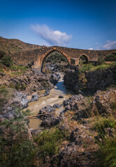 Ponte dei Saraceni. An ancient medieval bridge of Norman age located on the Simeto river. Adrano - Catania, in Sicily. Long exposure picture. June 2023