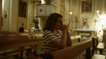 A young hispanic woman is praying inside an ornate christian church in italy.
