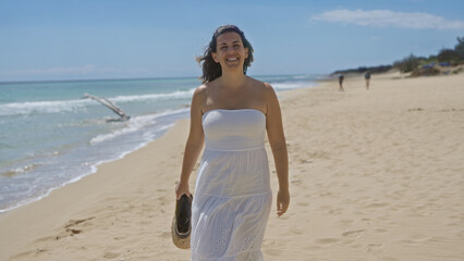 A beautiful young hispanic woman enjoys a sunny day at a serene beach in pescoluse, salento, puglia, italy, wearing a white dress and holding her sandals.