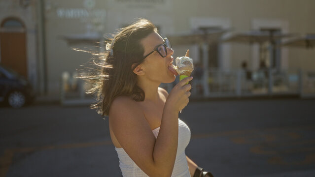 Fototapeta A beautiful young hispanic woman enjoying gelato on the sunny streets of gallipoli, puglia, italy, with windswept hair and a backdrop of charming italian architecture.