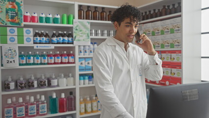 Handsome young man, a pharmacist, consults on the phone amidst various medicines in a modern drugstore interior.