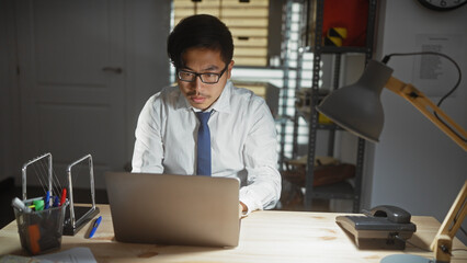 Asian man focused on working at computer in a modern office environment.