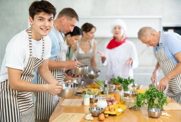 Young guy in apron learning to cook at cooking master class