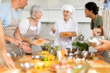 Enthusiastic young chef giving culinary classes to group of interested men and women of different...